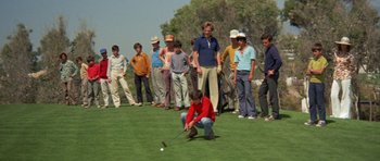 Movie still from “A Touch of Class” (1973), directed by Melvin Frank – A group of people standing around a man holding a golf club; Wide shot, High angle