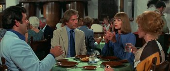 Movie still from “A Touch of Class” (1973), directed by Melvin Frank – A group of people sitting at a table with plates of food in front of them; Medium shot, Over the shoulder angle
