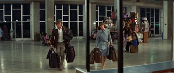 Movie still from “A Touch of Class” (1973), directed by Melvin Frank – A man and a woman walking through an airport carrying suitcases; Wide shot, High angle
