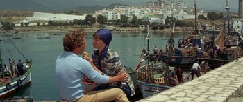 Movie still from “A Touch of Class” (1973), directed by Melvin Frank – A man and a woman sitting next to each other on a pier; Wide shot, High angle