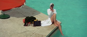 Movie still from “A Touch of Class” (1973), directed by Melvin Frank – A woman sitting on the side of a pool taking a picture; Wide shot, High angle
