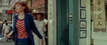 Movie still from “A Touch of Class” (1973), directed by Melvin Frank – A woman wearing a hat standing in front of a building; Medium shot, Over the shoulder angle