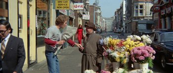 Movie still from “A Touch of Class” (1973), directed by Melvin Frank – A man is handing flowers to a woman on the street; Wide shot, Over the shoulder angle