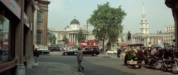 Movie still from “A Touch of Class” (1973), directed by Melvin Frank – A man walking across the street in front of a large building; Extreme Wide shot, High angle
