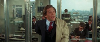 Movie still from “A Touch of Class” (1973), directed by Melvin Frank – A man in a suit and tie standing in front of other people; Medium shot, Low angle