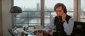 Movie still from “A Touch of Class” (1973), directed by Melvin Frank – A man sitting at a desk with a phone; Medium shot, Over the shoulder angle