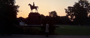 Movie still from “A Touch of Class” (1973), directed by Melvin Frank – A person standing in front of a statue of a man on a horse; Extreme Wide shot, Low angle