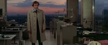 Movie still from “A Touch of Class” (1973), directed by Melvin Frank – A man in a trench coat standing in front of a table; Medium shot, Over the shoulder angle