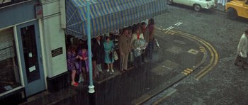 Movie still from “A Touch of Class” (1973), directed by Melvin Frank – A group of people standing under an umbrella on a rainy day; Wide shot, High angle