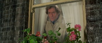 Movie still from “A Touch of Class” (1973), directed by Melvin Frank – A man looking out of a window with flowers in front of him; Medium shot, Low angle