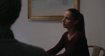Movie still from “A War” (2015), directed by Tobias Lindholm – A woman sitting in front of a painting looking off into the distance; Medium shot, Over the shoulder angle