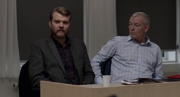 Movie still from “A War” (2015), directed by Tobias Lindholm – Two men sitting at a table with a cup of coffee in front of them; Medium shot, Over the shoulder angle