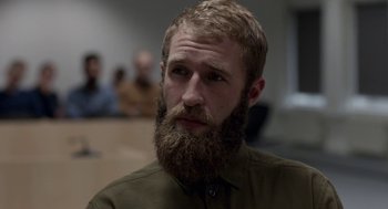 Movie still from “A War” (2015), directed by Tobias Lindholm – A man with a long beard is sitting in front of a group of people; Close Up shot, Over the shoulder angle