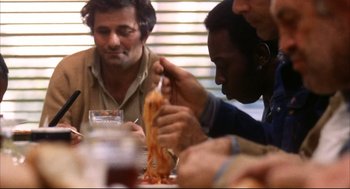 Movie still from “A Woman Under the Influence” (1974), directed by John Cassavetes – A group of people sitting at a table eating pizza; Medium shot, Over the shoulder angle