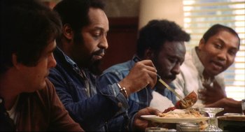 Movie still from “A Woman Under the Influence” (1974), directed by John Cassavetes – A group of people sitting at a table eating food; Medium shot, Over the shoulder angle