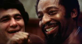Movie still from “A Woman Under the Influence” (1974), directed by John Cassavetes – A man with a long beard smiling next to a woman; Extreme Close Up shot, Low angle