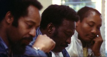 Movie still from “A Woman Under the Influence” (1974), directed by John Cassavetes – Two men are sitting in a room and one of them has his hand on his face; Close Up shot, High angle