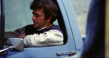 Movie still from “A Woman Under the Influence” (1974), directed by John Cassavetes – A man sitting in the drivers seat of a blue car; Close Up shot, High angle