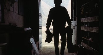 Movie still from “A Woman Under the Influence” (1974), directed by John Cassavetes – A man walking through a door way holding a bag; Wide shot, Low angle