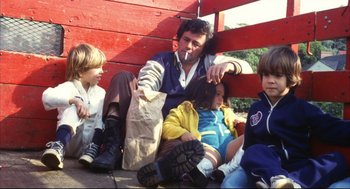 Movie still from “A Woman Under the Influence” (1974), directed by John Cassavetes – A group of people sitting next to each other on the ground; Medium shot, High angle