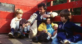 Movie still from “A Woman Under the Influence” (1974), directed by John Cassavetes – A group of people sitting next to each other on the ground; Medium shot, High angle