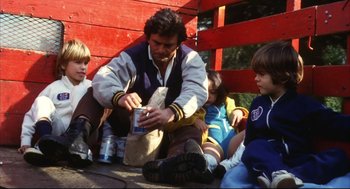 Movie still from “A Woman Under the Influence” (1974), directed by John Cassavetes – A group of children sitting on the ground with a man holding something; Medium shot, Low angle