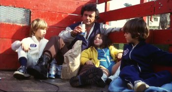 Movie still from “A Woman Under the Influence” (1974), directed by John Cassavetes – A group of people sitting next to each other on the ground; Medium shot, High angle