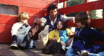 Movie still from “A Woman Under the Influence” (1974), directed by John Cassavetes – A man sitting on the ground next to two children; Medium shot, High angle