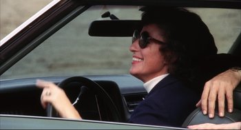 Movie still from “A Woman Under the Influence” (1974), directed by John Cassavetes – A man in a suit and sunglasses driving a car; Close Up shot, Low angle
