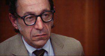 Movie still from “A Woman Under the Influence” (1974), directed by John Cassavetes – An older man wearing glasses and a suit; Close Up shot, Over the shoulder angle