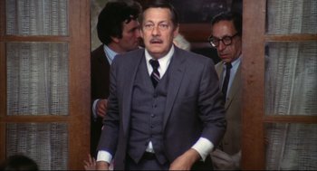 Movie still from “A Woman Under the Influence” (1974), directed by John Cassavetes – A man in a suit and tie standing next to two other men; Medium shot, High angle