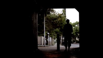 Movie still from “Absentia” (2011), directed by Mike Flanagan – A person standing on the side of a road near trees; Wide shot, Low angle