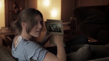 Movie still from “Absentia” (2011), directed by Mike Flanagan – A woman sitting on a couch holding a book; Medium shot, Over the shoulder angle