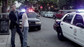 Movie still from “Absentia” (2011), directed by Mike Flanagan – A man standing on the side of the road near parked police cars; Medium shot, Over the shoulder angle