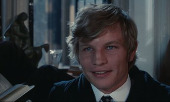 Movie still from “Accident” (1967), directed by Joseph Losey – A young man in a suit and tie smiling for the camera; Close Up shot, Over the shoulder angle
