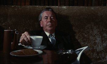 Movie still from “Accident” (1967), directed by Joseph Losey – An older man sitting at a table drinking coffee; Medium shot, Low angle