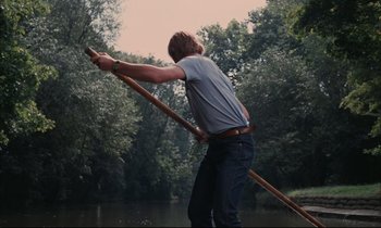 Movie still from “Accident” (1967), directed by Joseph Losey – A man holding onto a wooden stick while standing in the water; Wide shot, Low angle