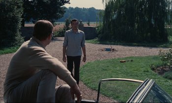 Movie still from “Accident” (1967), directed by Joseph Losey – Two men standing on a gravel road near a tree; Wide shot, High angle