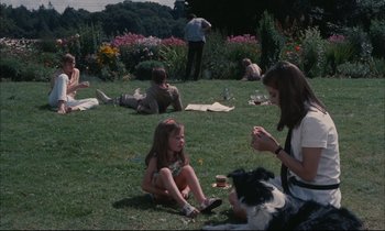 Movie still from “Accident” (1967), directed by Joseph Losey – A group of people sitting in the grass with a black and white dog; Wide shot, High angle