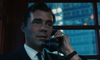 Movie still from “Accident” (1967), directed by Joseph Losey – A man wearing a suit and tie talking on a phone; Close Up shot, Low angle