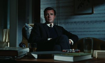 Movie still from “Accident” (1967), directed by Joseph Losey – A man in a suit sitting at a table; Medium shot, Low angle