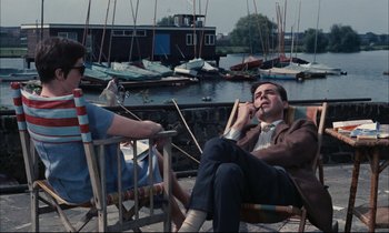 Movie still from “Accident” (1967), directed by Joseph Losey – A man and a woman sitting on a chair next to a body of water; Medium shot, High angle