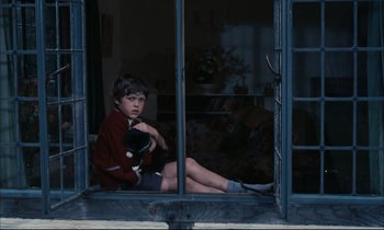 Movie still from “Accident” (1967), directed by Joseph Losey – A boy sitting on a window ledge holding a stuffed animal; Medium shot, High angle