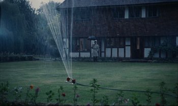 Movie still from “Accident” (1967), directed by Joseph Losey – A man holding an umbrella is standing in the rain; Extreme Wide shot, High angle