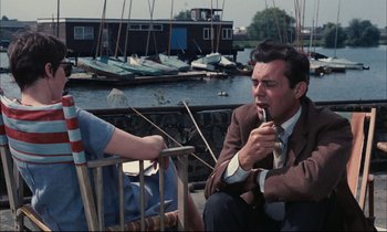 Movie still from “Accident” (1967), directed by Joseph Losey – A man and a woman sitting next to each other on a dock; Medium shot, High angle