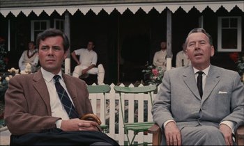 Movie still from “Accident” (1967), directed by Joseph Losey – Two men sitting on a lawn chair in front of a house; Medium shot, Low angle