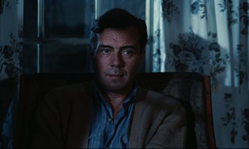 Movie still from “Accident” (1967), directed by Joseph Losey – A person sitting in a chair wearing a jacket; Close Up shot, Over the shoulder angle