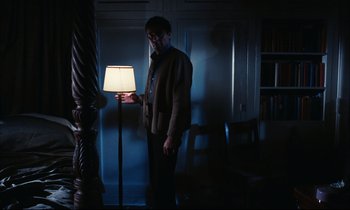 Movie still from “Accident” (1967), directed by Joseph Losey – A man standing next to a lamp in a dark room; Wide shot, Low angle