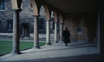 Movie still from “Accident” (1967), directed by Joseph Losey – A person walking down a sidewalk near a building; Extreme Wide shot, High angle