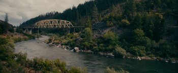 Movie still from “Acidman” (2022), directed by Alex Lehmann – A bridge over a body of water surrounded by trees and rocks; Extreme Wide shot, High angle
